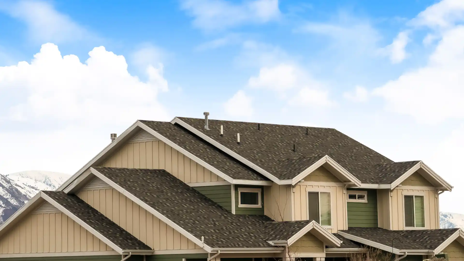 A two-story house with a dark roof and beige siding under a blue sky