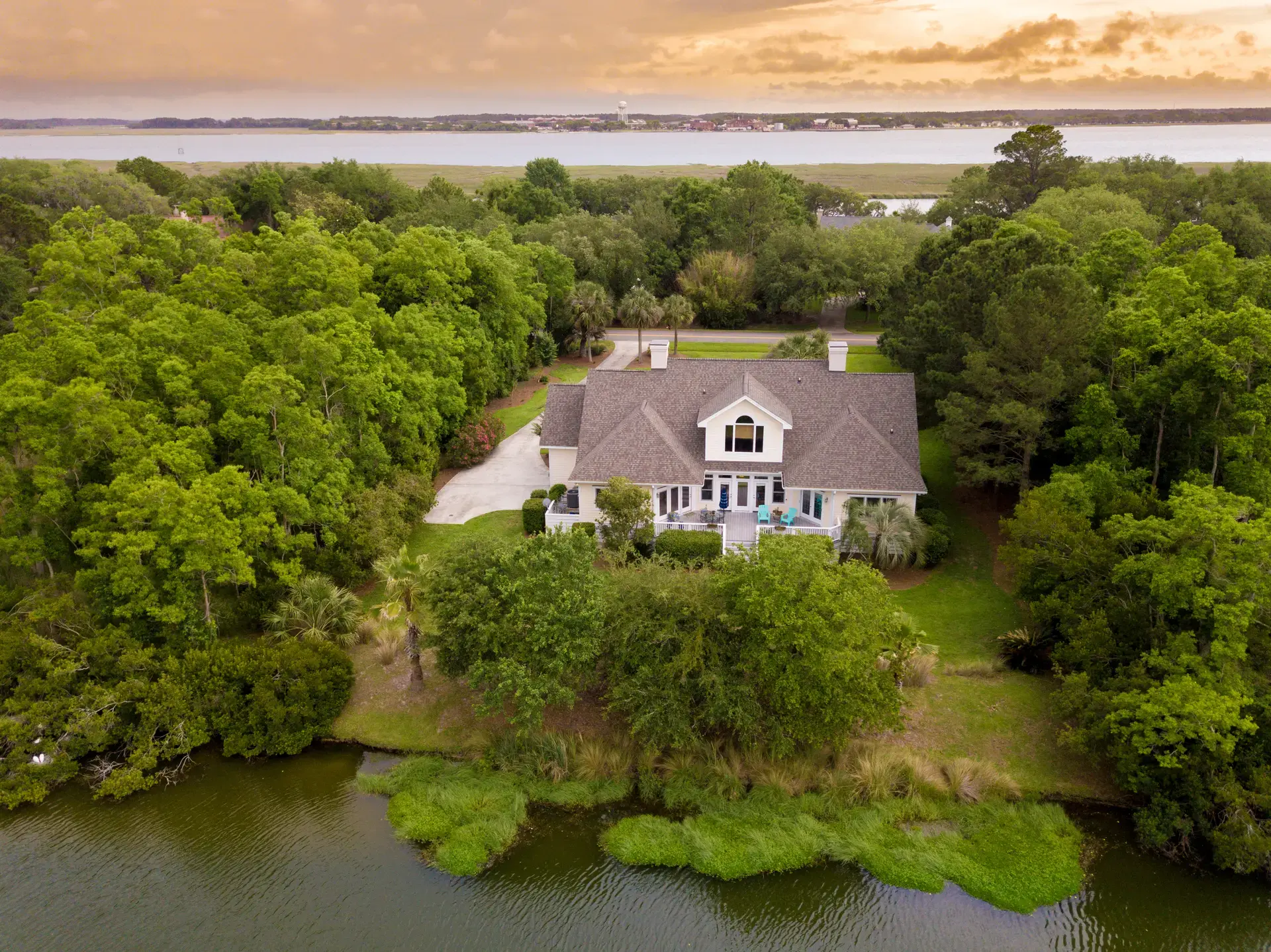 Aerial view of a large white house with a brown roof, surrounded by trees and a body of water