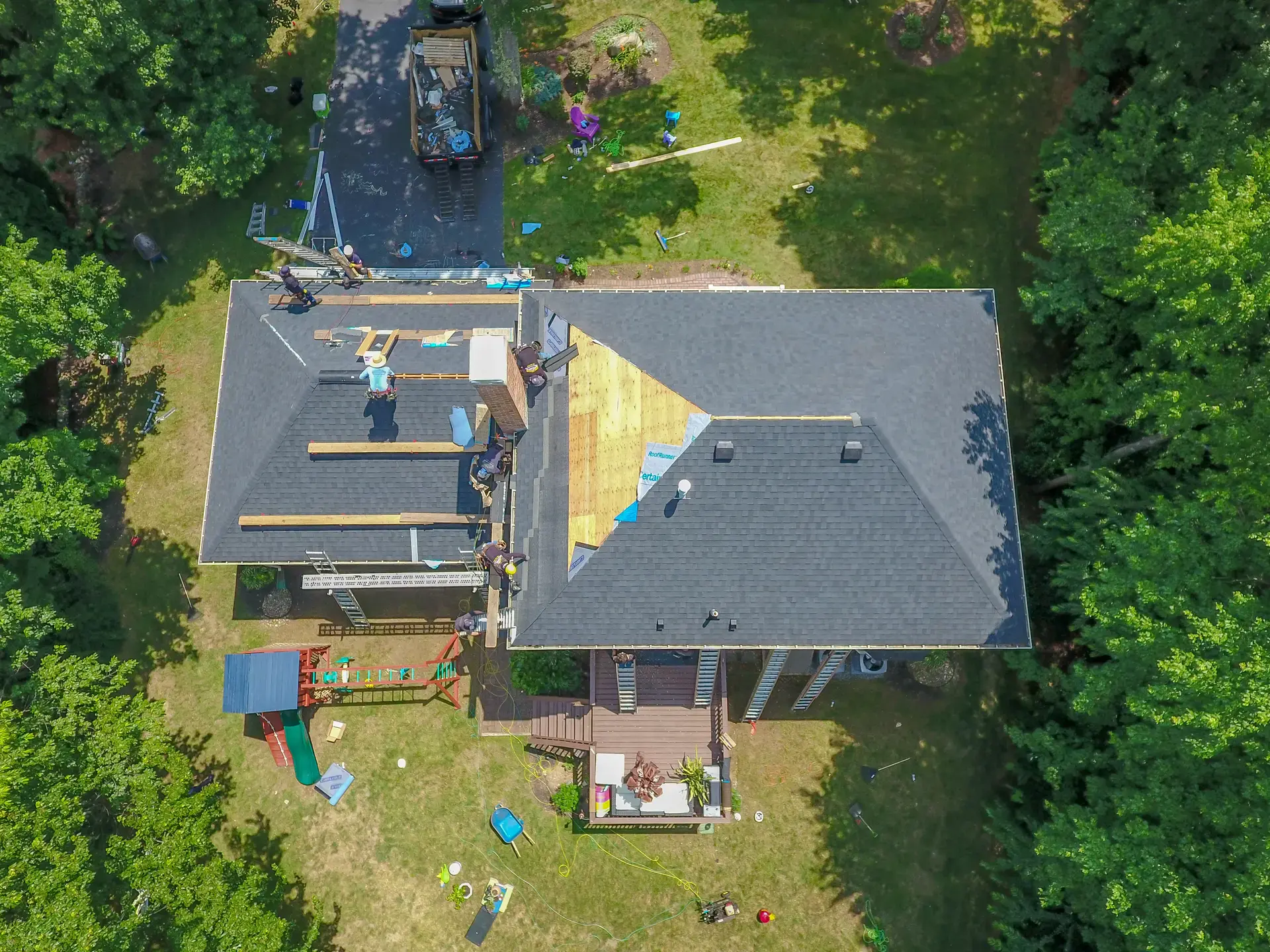 Aerial view of a house under construction, with a backyard and trees surrounding it