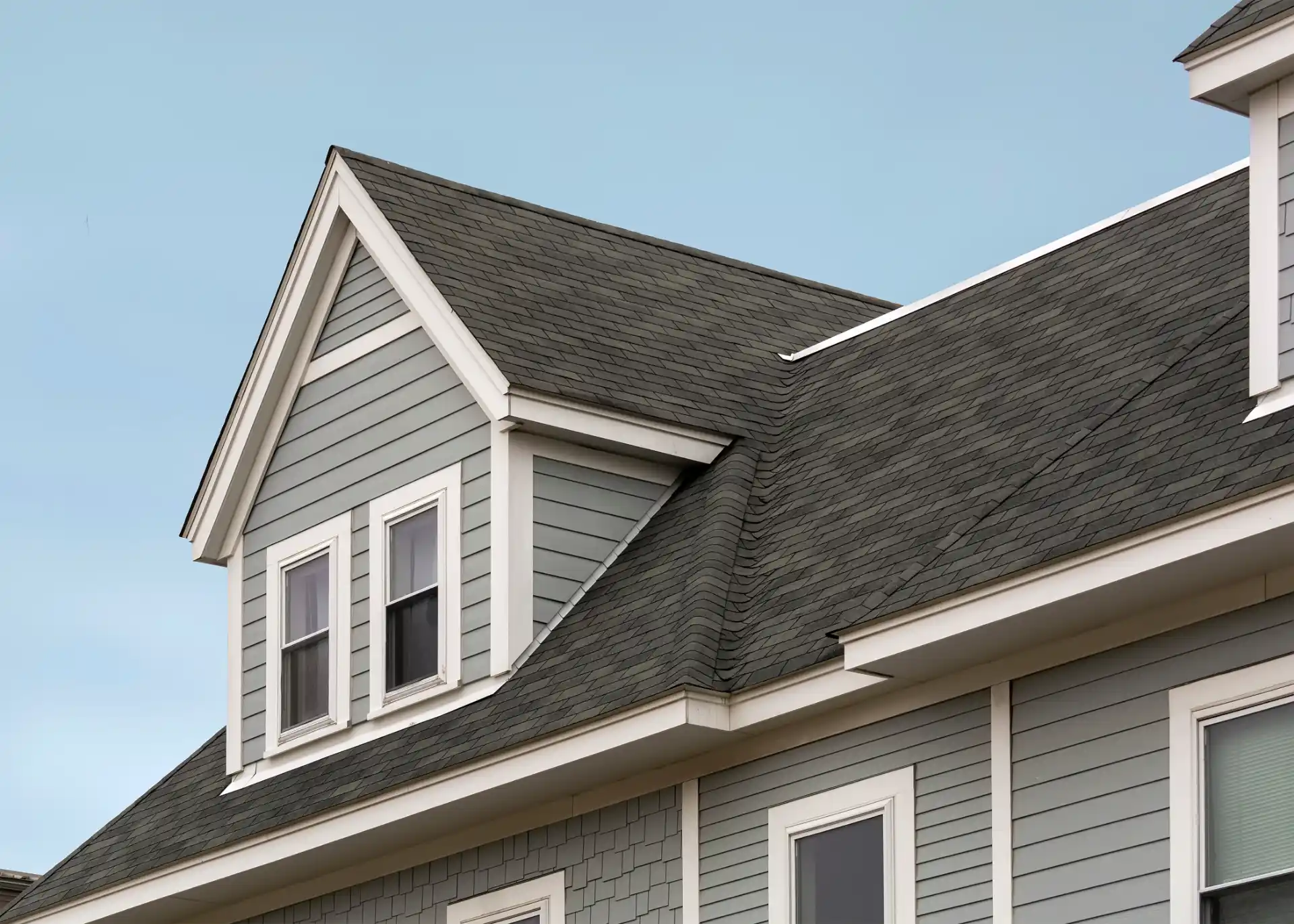 A gray house with white trim and a dark roof, set against a clear blue sky