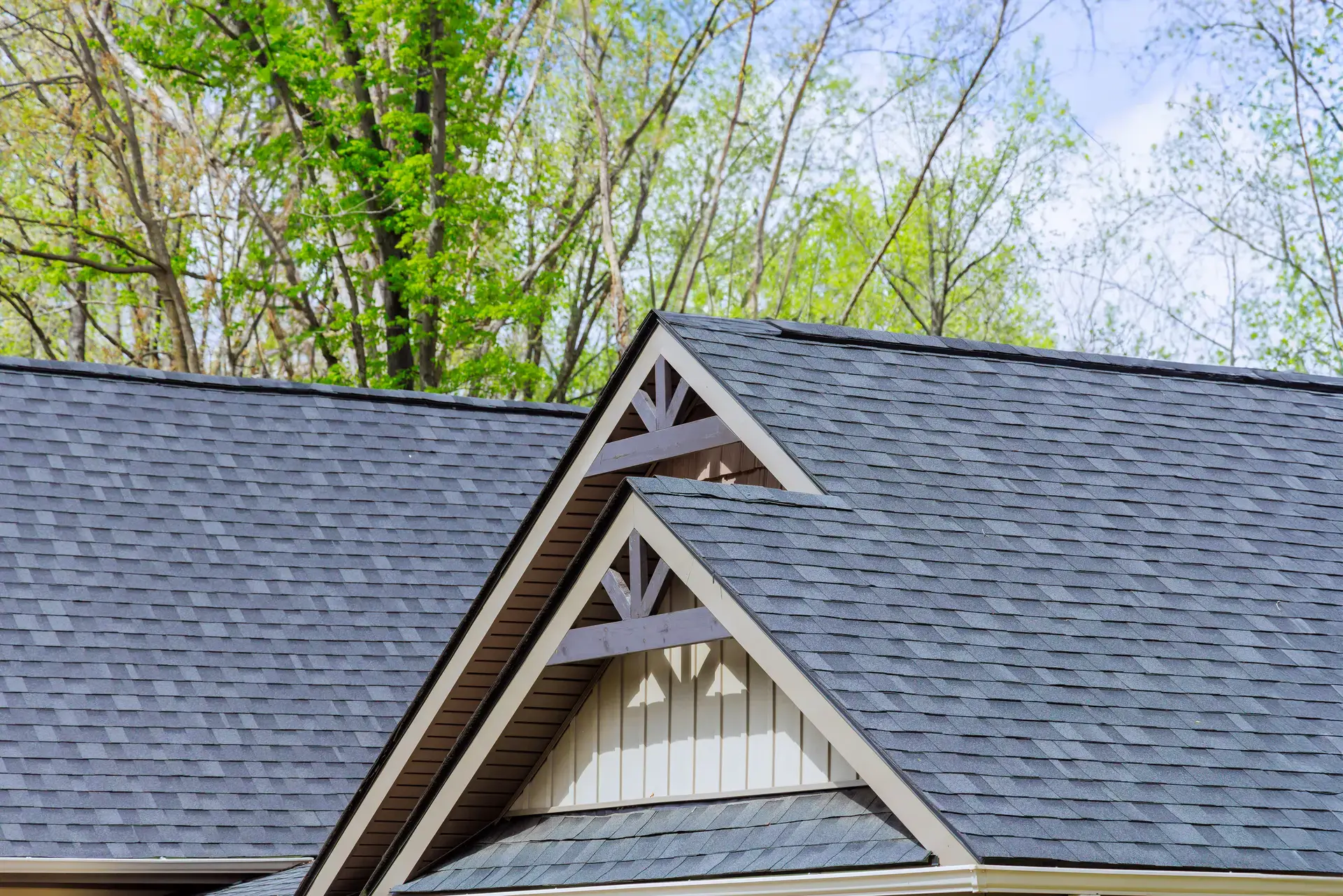 A gray roof with white trim and triangular gables, set against a backdrop of trees